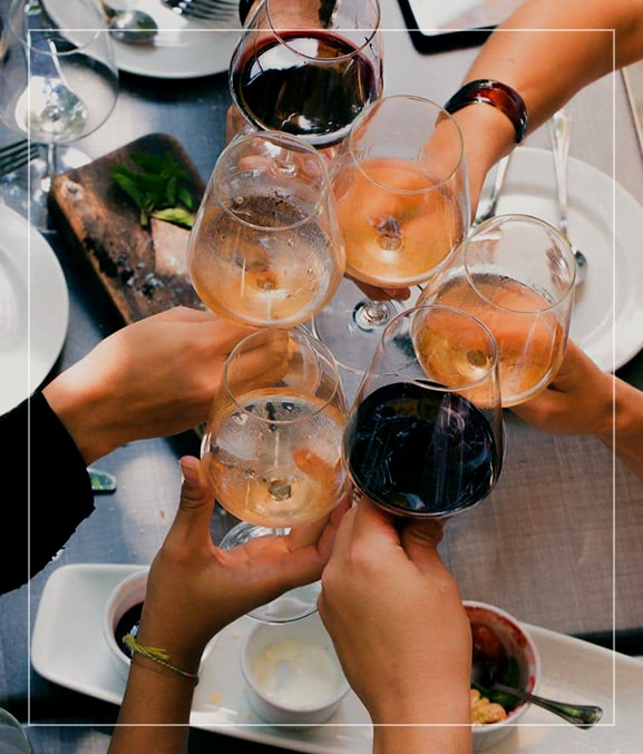Group of friends sitting at restaurant table toasting with wine