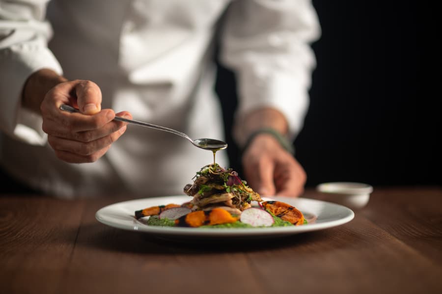 Chef pouring sauce from spoon onto plated meal